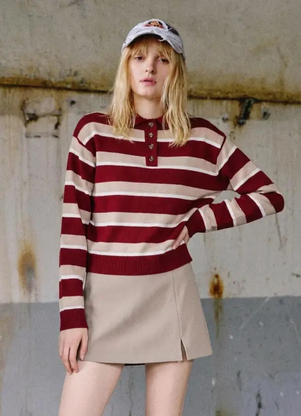 A Woman Stands Confidently In A Casual Striped Sweater And Skirt Against An Industrial Textured Wall Backdrop